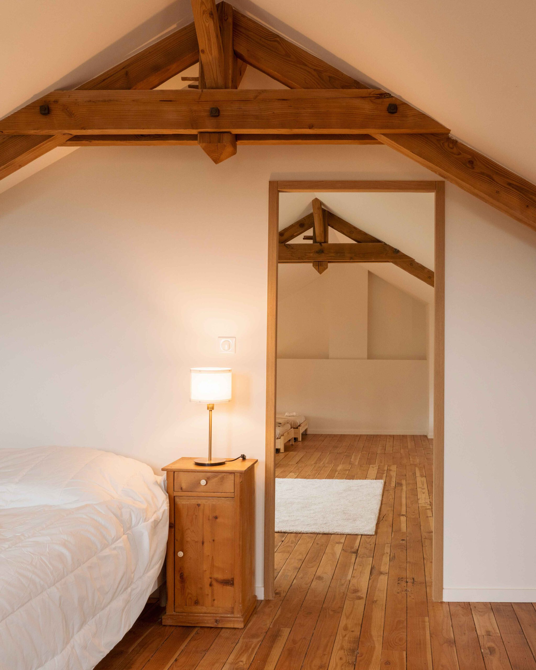 Photographie d'un ensemble de chambre en soupente à la suite du travail de l'architecte en rénovation de maison dans le Beaujolais. Les teintes sont douces et le bois domine.